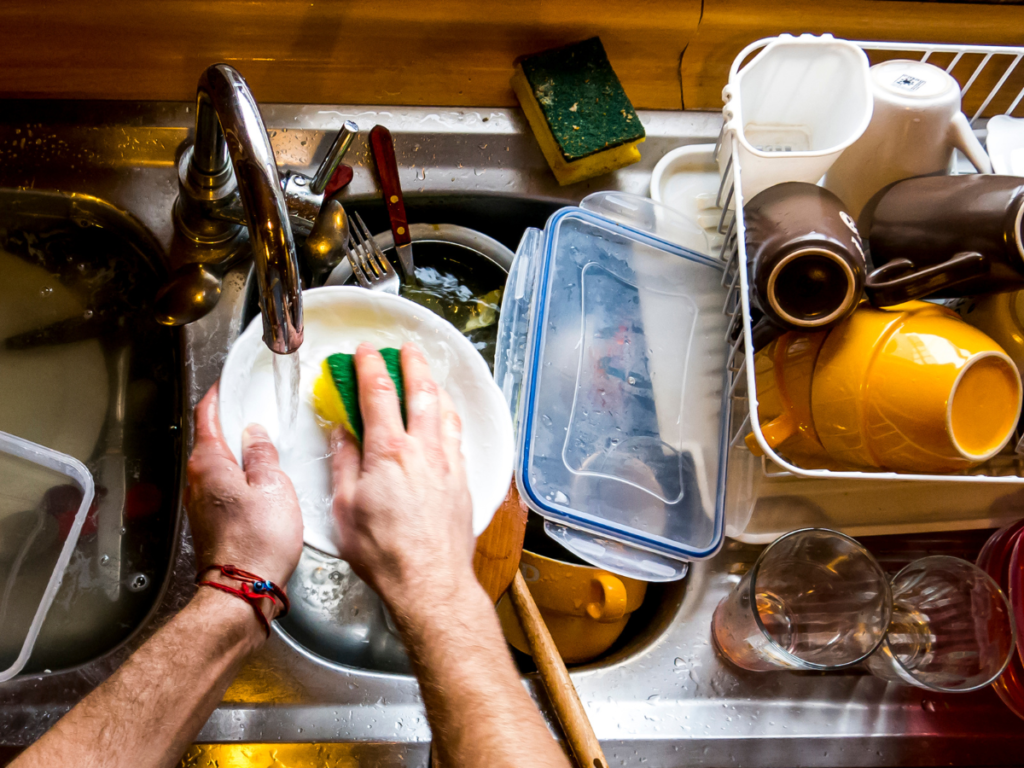 close up shot of someone cleaning dishes in a cluttered kitchen sink