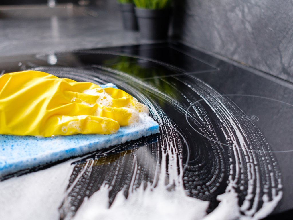 up close shot of someone wiping down a stovetop with a yellow glove and blue sponge