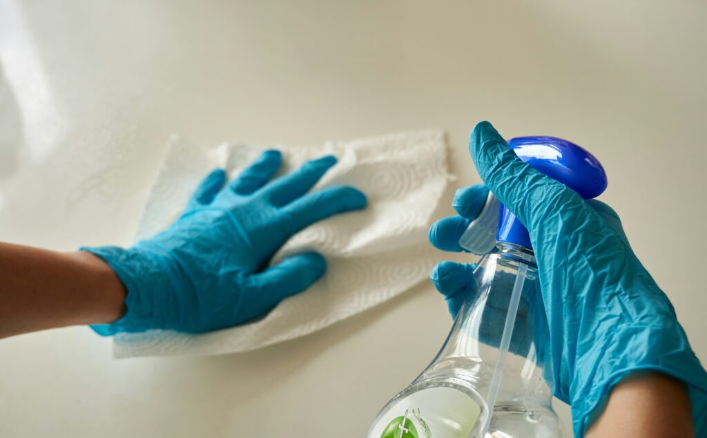 blue gloved hands spraying a surface cleaning and wiping a countertop