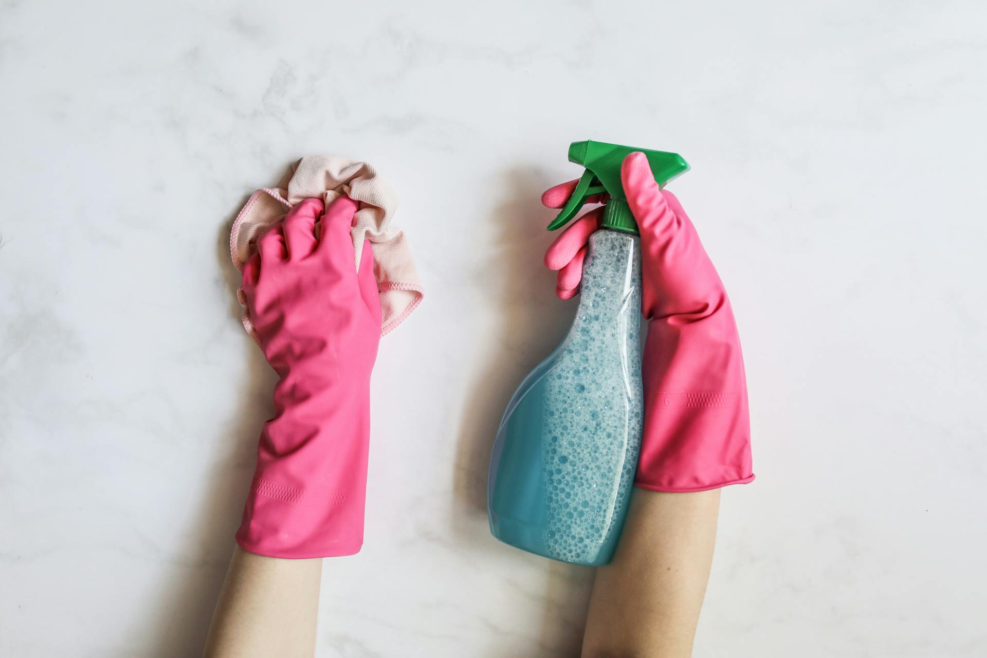pink gloved hands holding cleaning rag and window cleaner