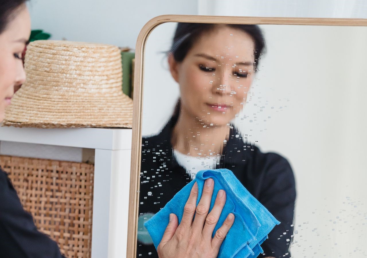 woman in black shirt cleaning a mirror with a blue towel